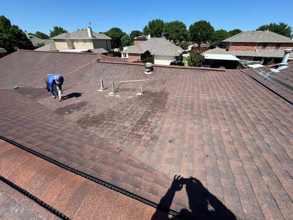 Roofer inspecting damaged asphalt shingles on a residential roof.