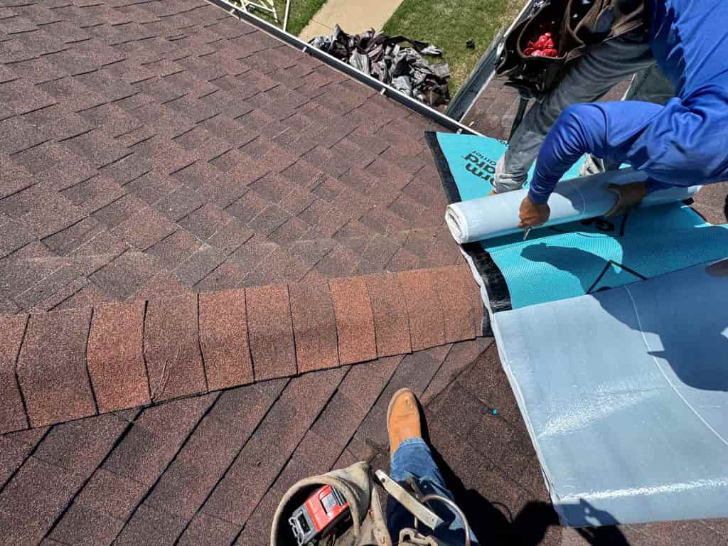 Roofers applying protective underlayment around shingles during residential roof leak repair.