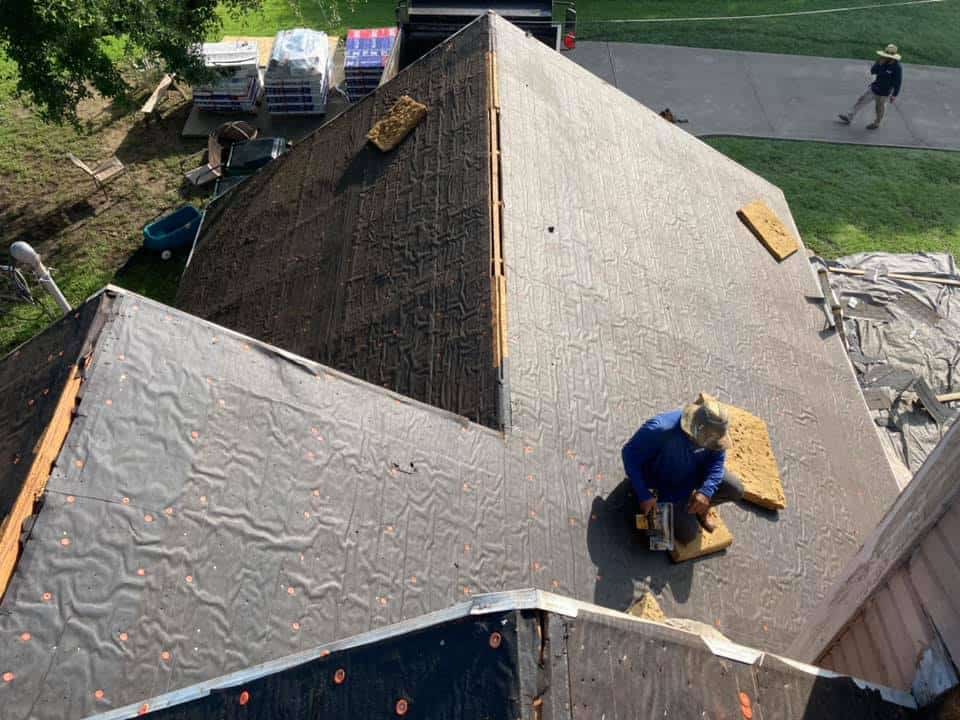 Roofer working on exposed roof decking and underlayment during a residential roof replacement.