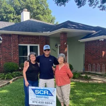 SCR Roofing representative standing with two homeowners outside their brick home.
