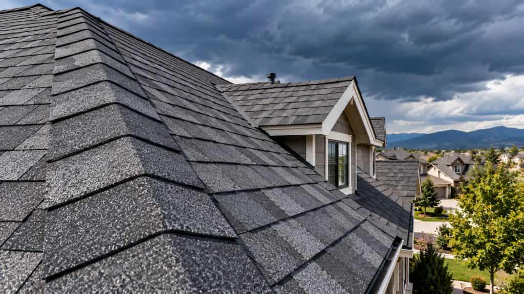 Close-up of dark architectural laminate shingles on a residential roof beneath storm clouds.