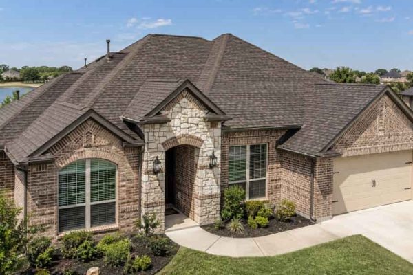 Brick home with a large architectural shingle roof featuring multiple slopes, valleys, and ridges.